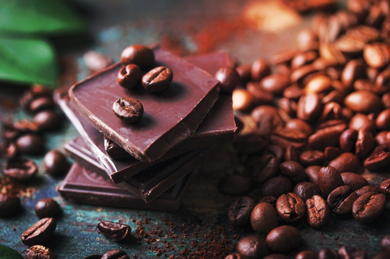 pieces of chocolate bars stacked up with coffee beans scattered on and around the bars